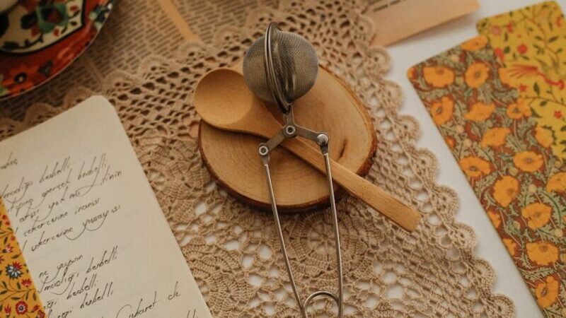 Delicate tea setup on lace, featuring a wooden spoon, infuser, and vintage decor.
